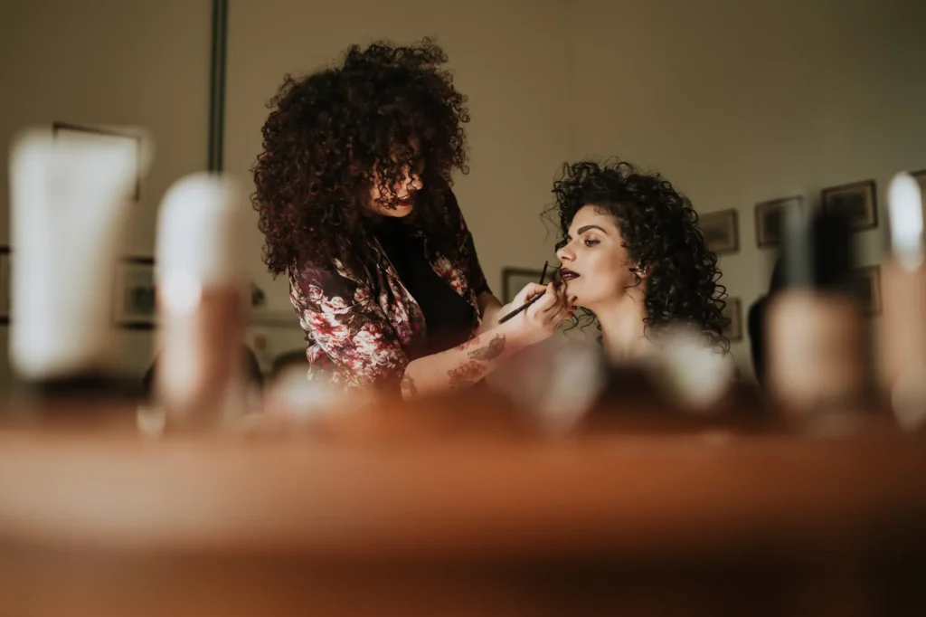 Trucco da sposa: una truccatrice applica il rossetto a una donna con capelli ricci, preparandola per il giorno del matrimonio.