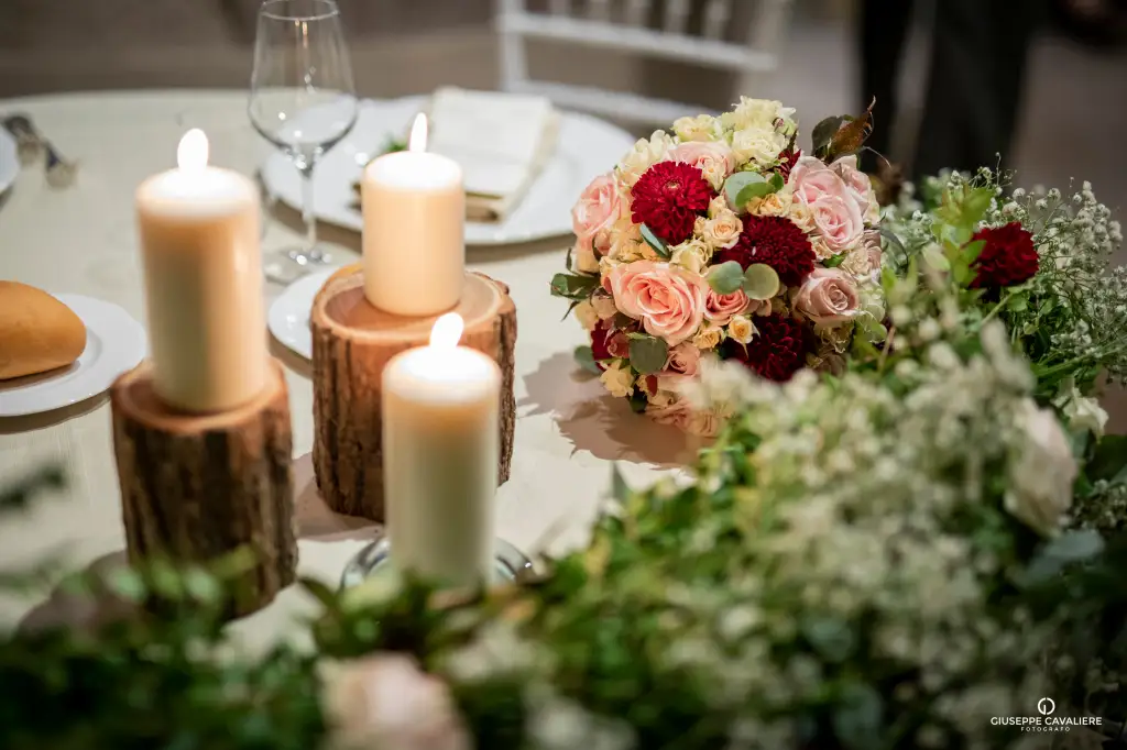 Centrotavola per matrimonio con candele su basi rustiche e un bouquet di rose rosse e rosa, circondato da gipsofila.